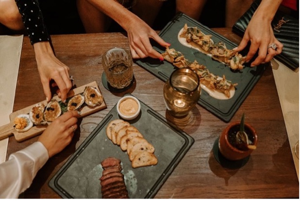 Small shared plates on cutting boards with guests reaching in, featuring the culinary experience at Meat Market Tampa.